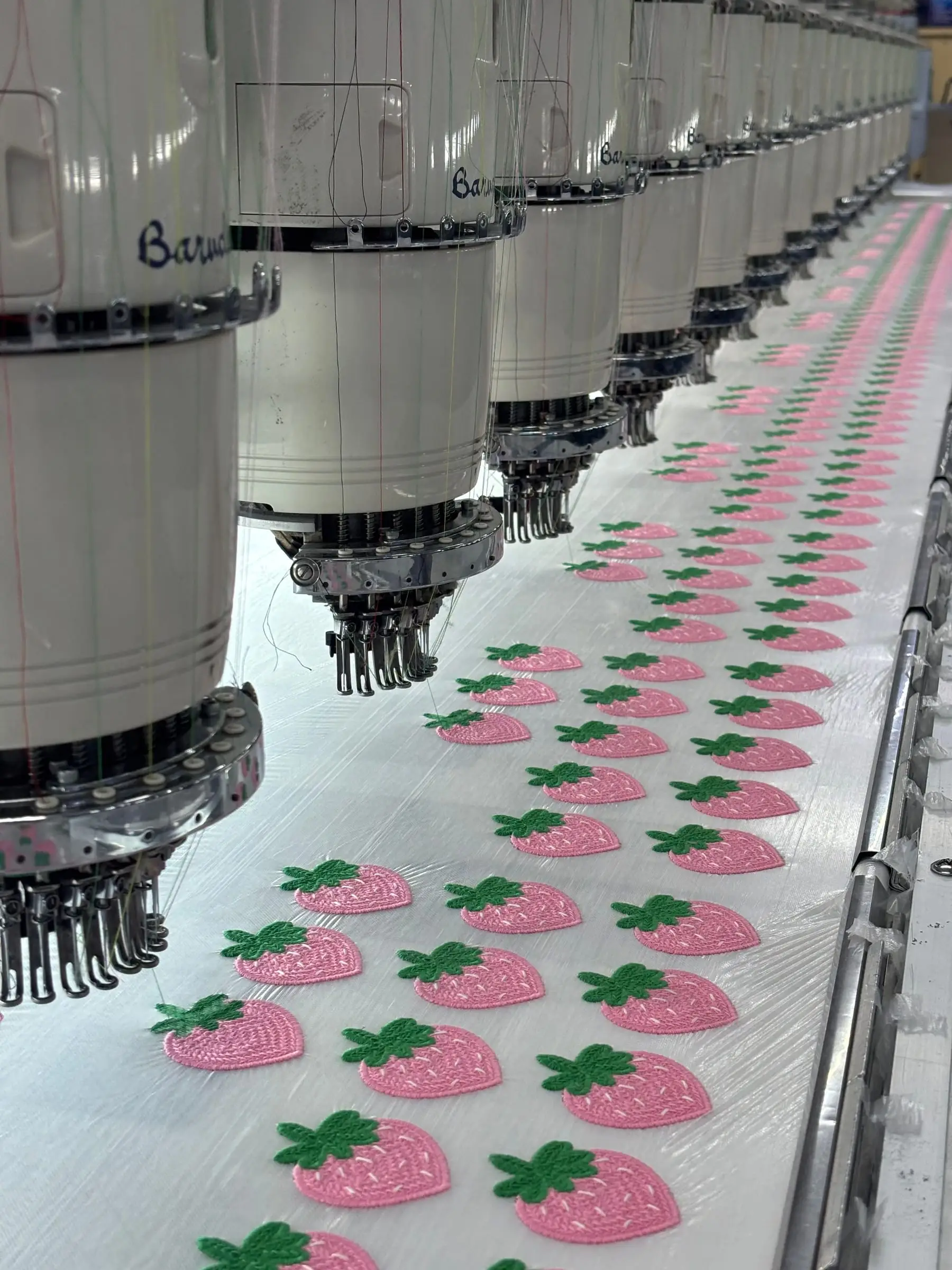 A multi-head embroidery machine mid-run, stitching a repeating motif across a full width of backing fabric.