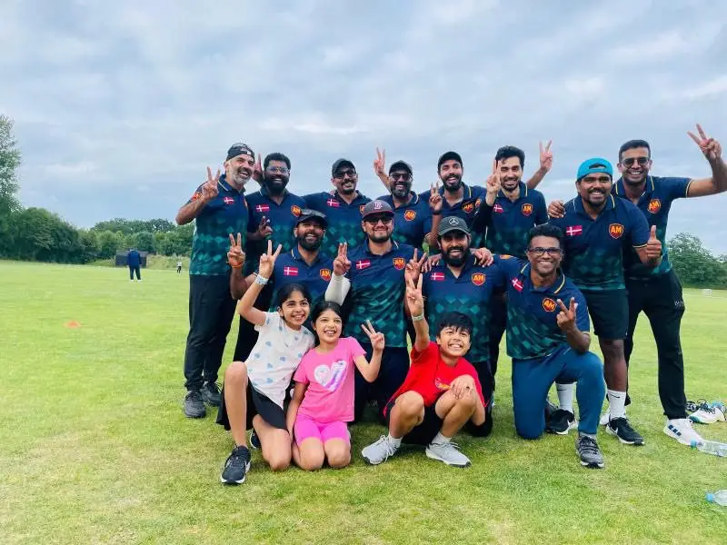 A cricket team in matching navy-and-green kit celebrating on the field with young supporters.