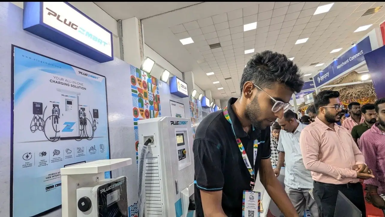 Plugzmart staff in black branded polos demonstrating products to visitors at an expo stand.