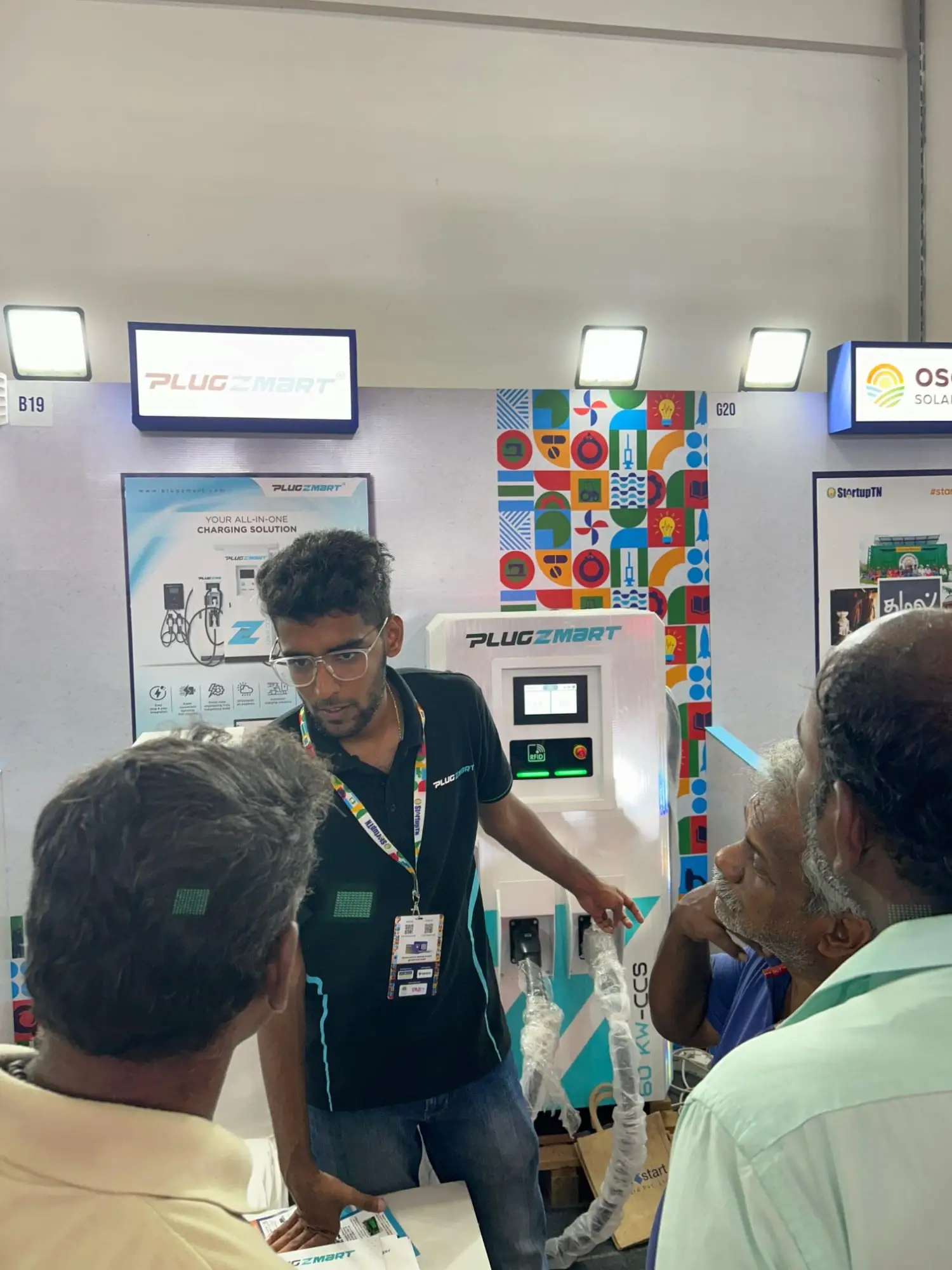 A Plugzmart team member in the black branded polo explaining an EV charger to visitors at the expo stand.