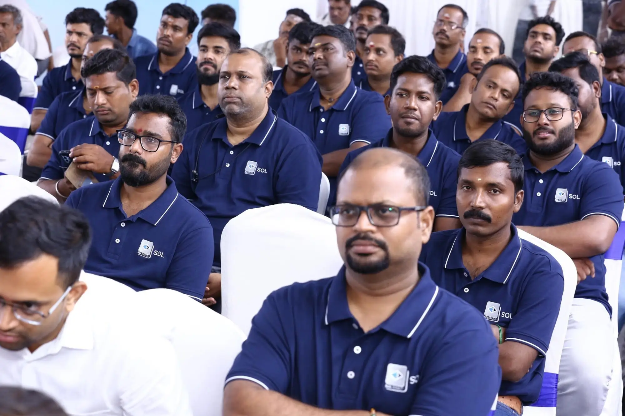 Rows of SOL Group staff seated at the ceremony in navy SOL polos, the logo embroidered at the chest.