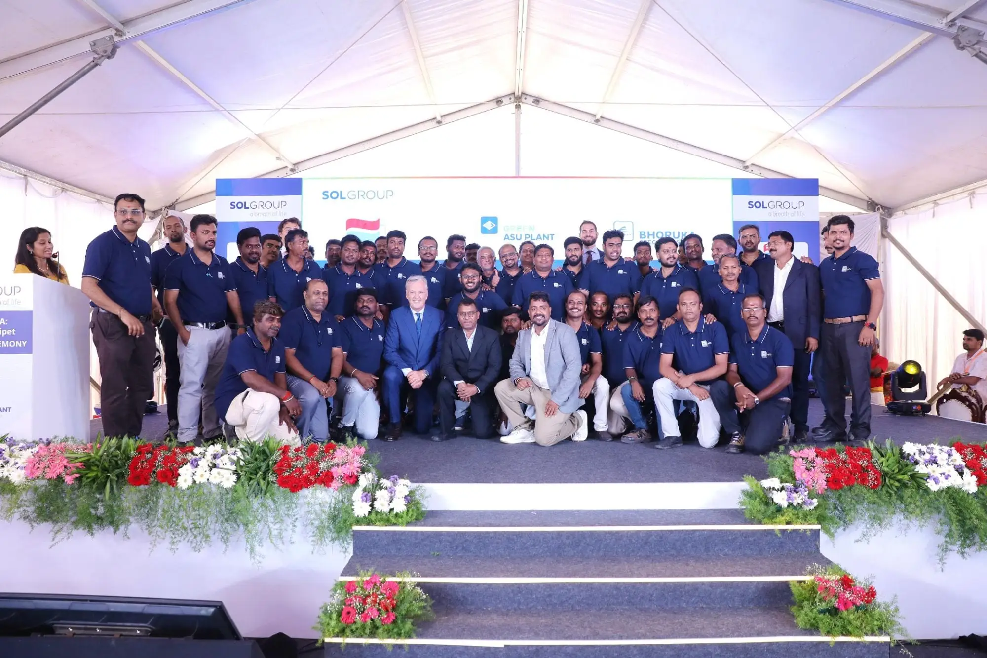 The SOL Group team on stage at a plant ceremony, everyone in the navy SOL polo with white tipping.