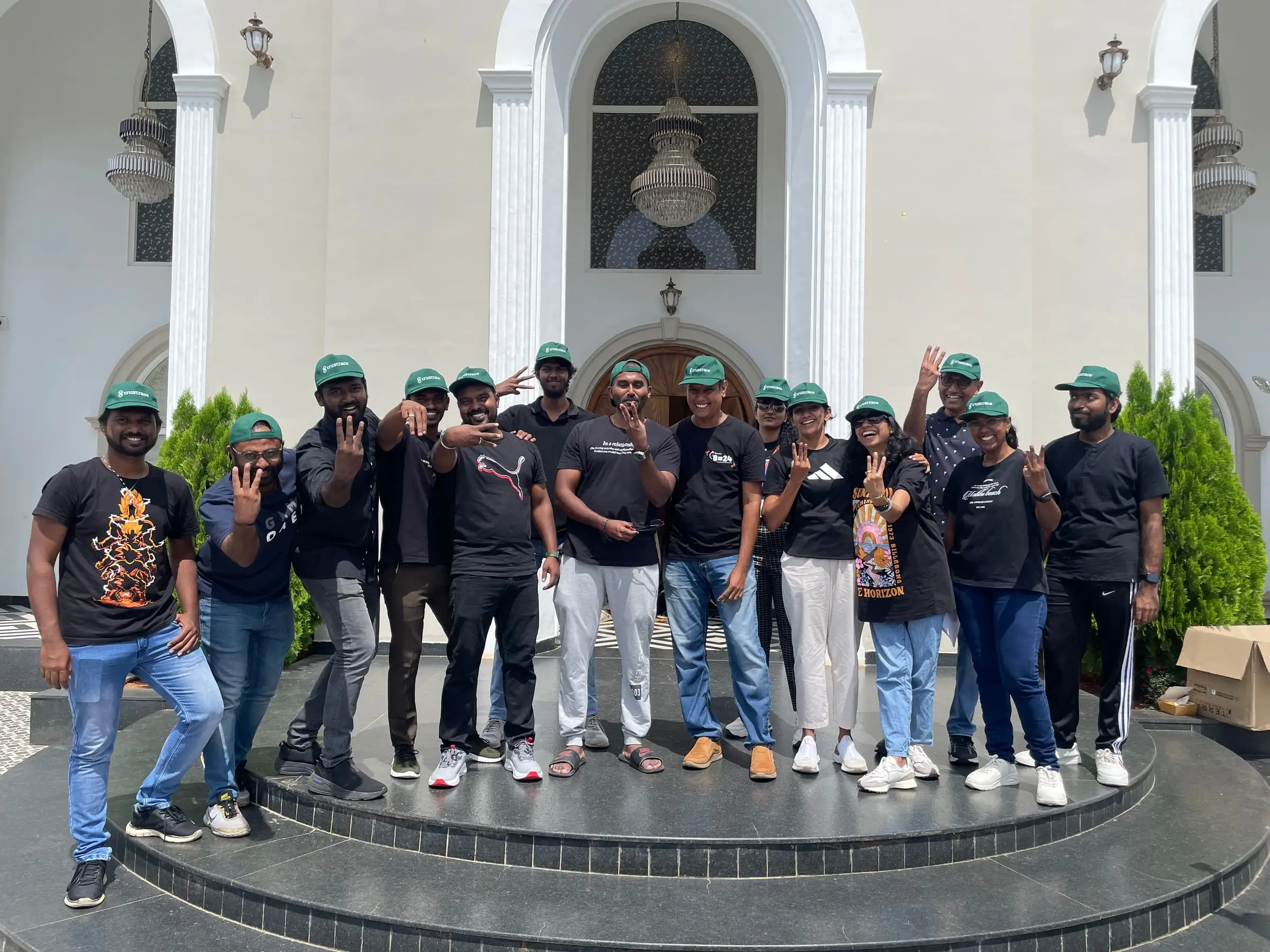 The team again in black tees and green caps, waving on the front steps.