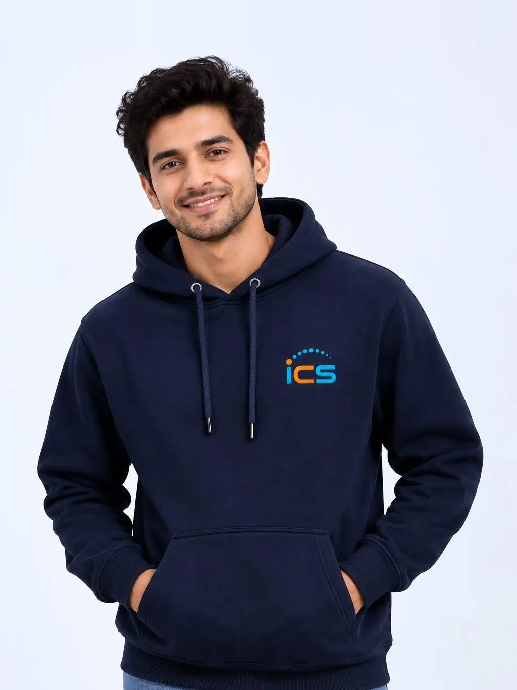 A model in a navy pullover hoodie, hands in the kangaroo pocket, the ICS logo embroidered in blue and orange at the chest.