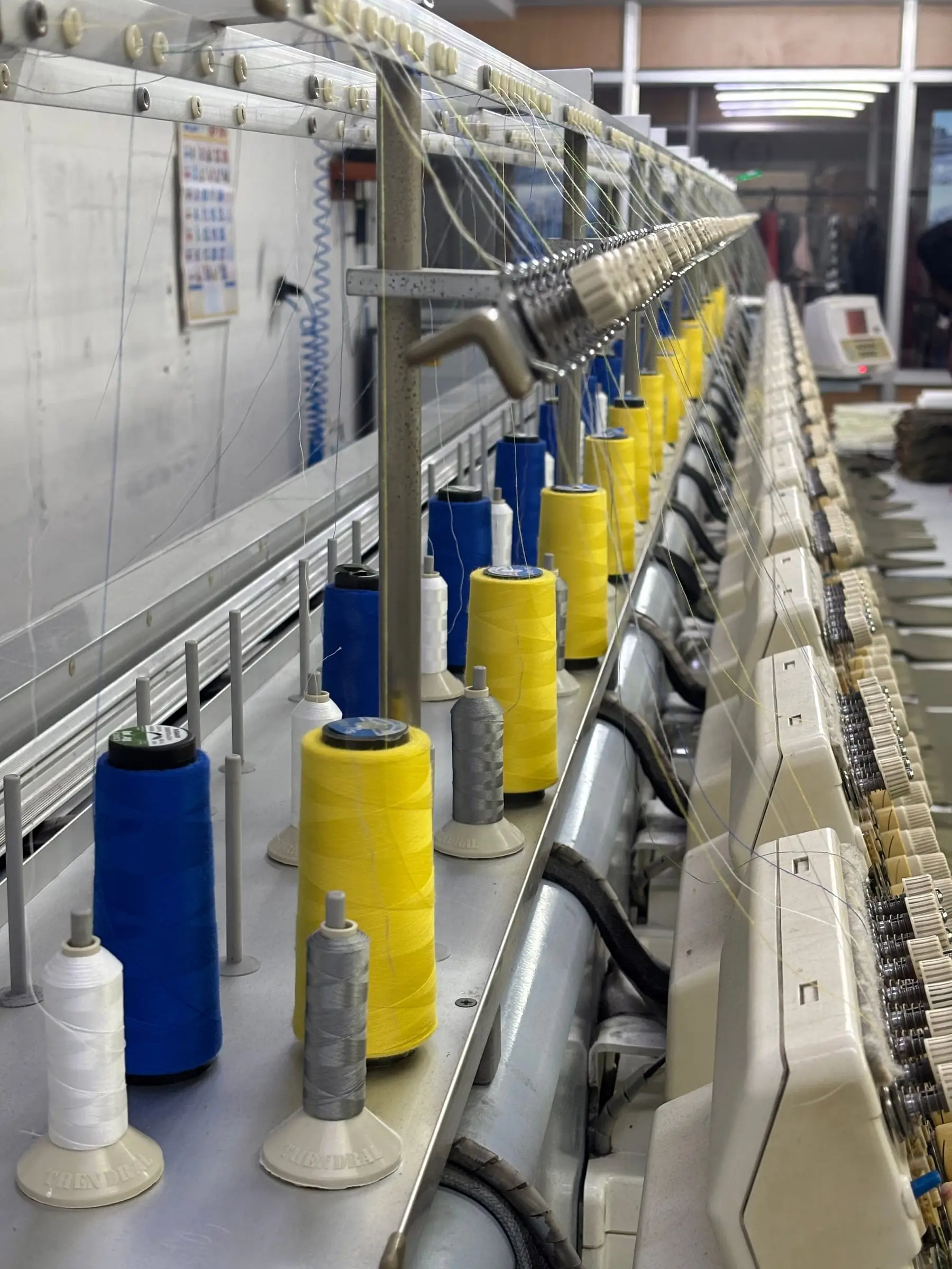 A run of thread cones mounted along the machine bed, colour-matched to the approved artwork.